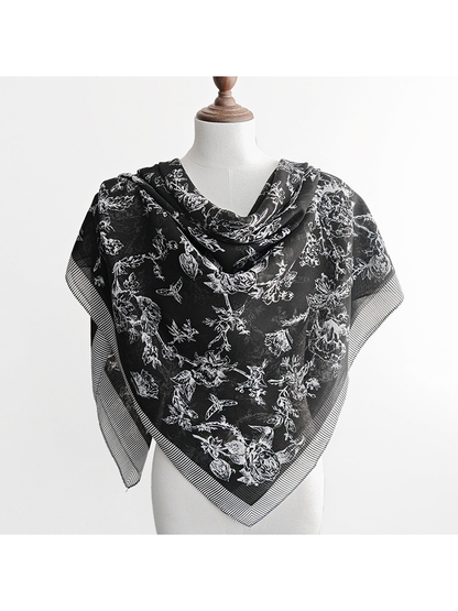 Black patterned scarf styled as a triangular front drape on a dress form