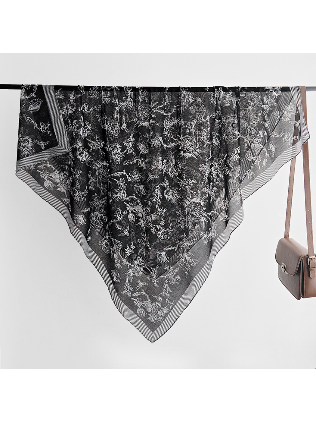 Black square scarf draped over a rail with white floral, bird and butterfly motifs