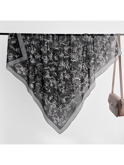 Black square scarf draped over a rail with white floral, bird and butterfly motifs
