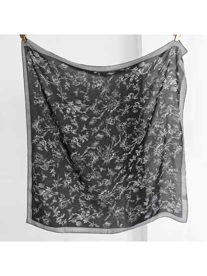 Black square scarf hanging open with white floral, bird and butterfly motifs and a striped border
