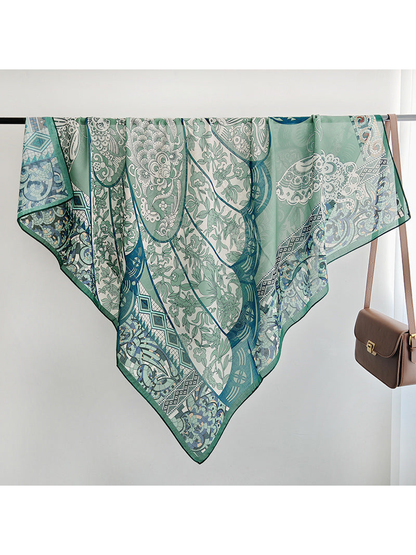 Green patterned square scarf draped over a rail, showing its semi-sheer appearance