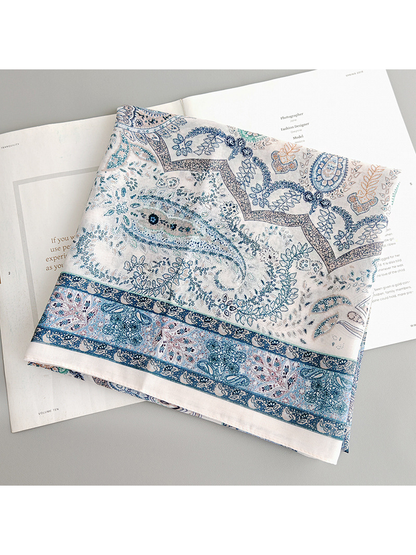 Folded blue paisley scarf showing the patterned border and ivory edge