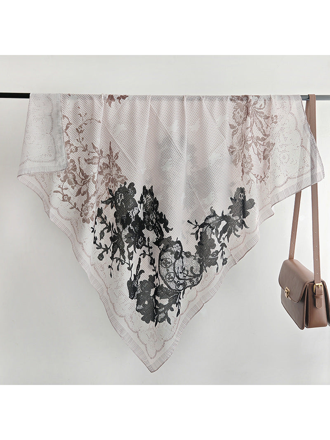 Square floral scarf draped over a display rail beside a handbag