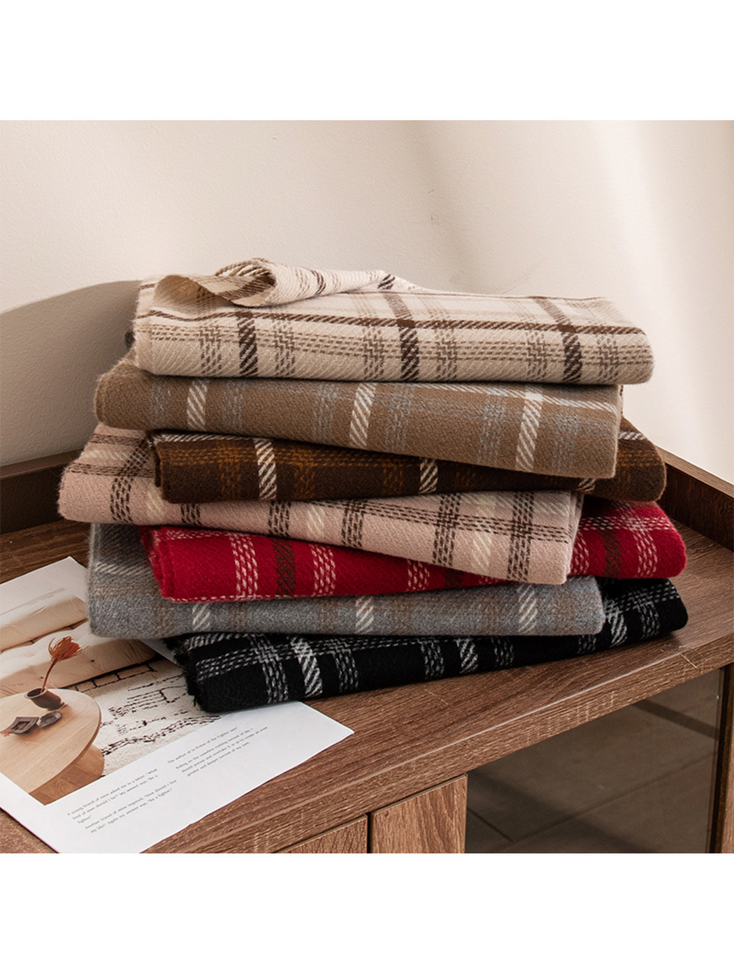 Assorted plaid fringe scarves stacked on a wooden cabinet