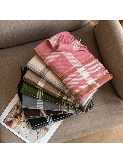 Seven plaid fringe scarf colorways stacked on a neutral sofa