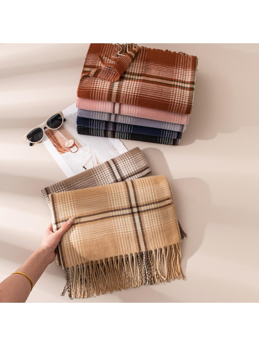 Assorted plaid scarves stacked with a camel scarf held in the foreground