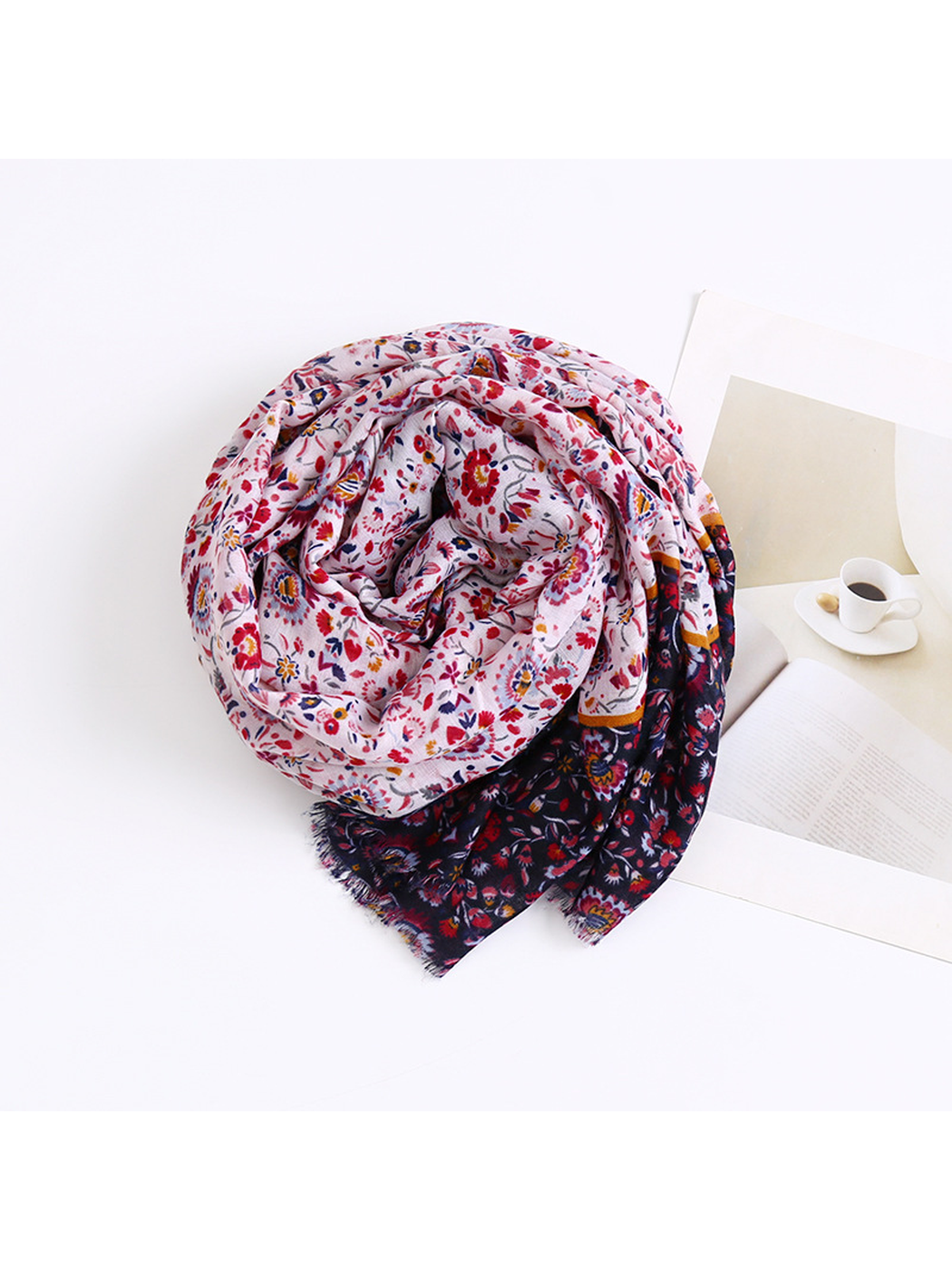 Floral scarf arranged in a loose coil beside a book and cup print