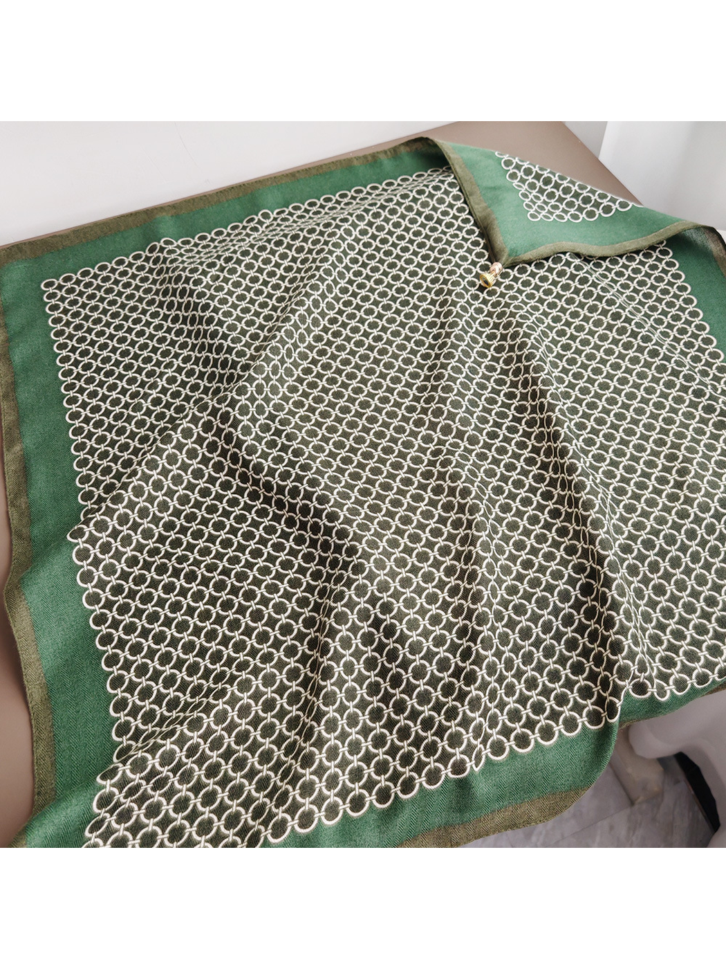 Green square scarf laid open to show the broad border and central ring pattern