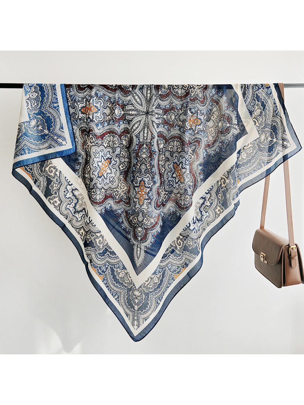 Navy and ivory paisley square scarf draped over a rail beside a handbag
