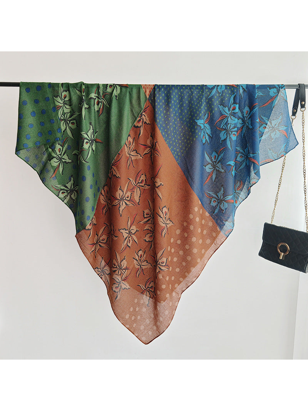 Multicolor square scarf draped across a clothing rail beside a black handbag