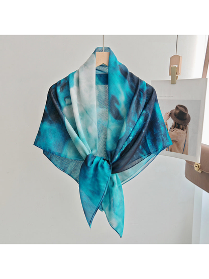 Teal, aqua and navy abstract square scarf tied at the front on a hanger