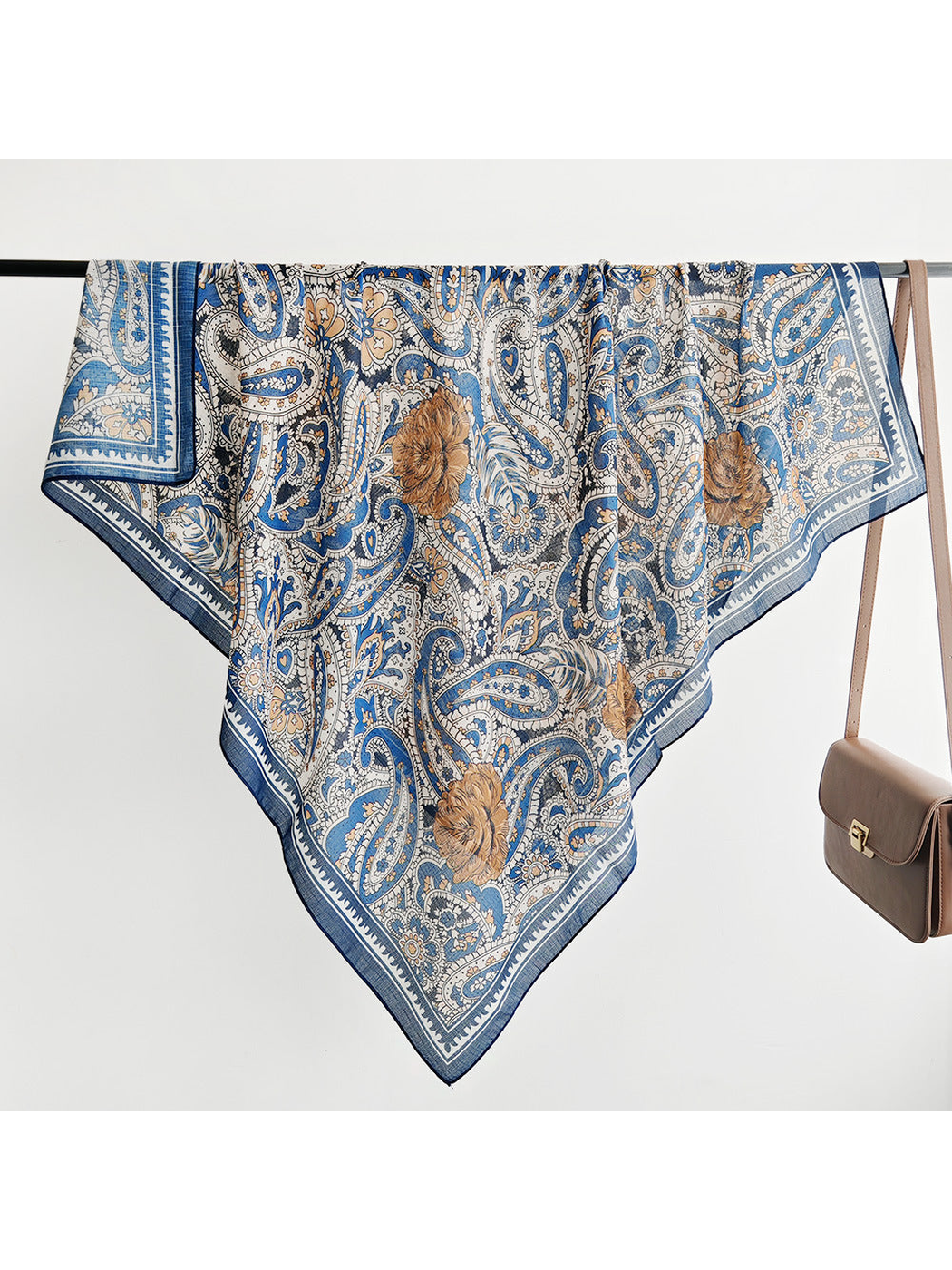 Blue, cream and brown paisley square scarf displayed across a rail