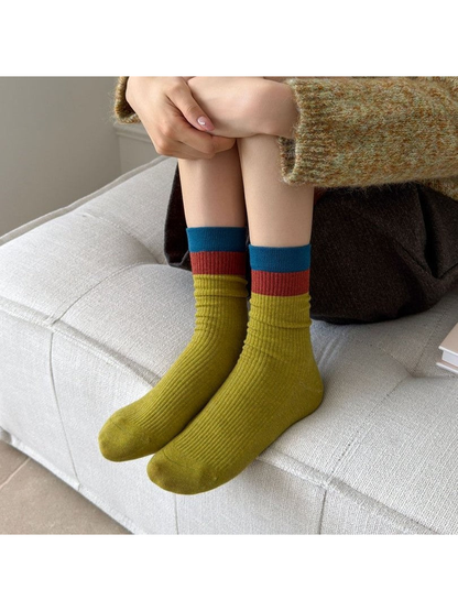 Army Green ribbed crew socks with red and teal cuff bands worn while seated
