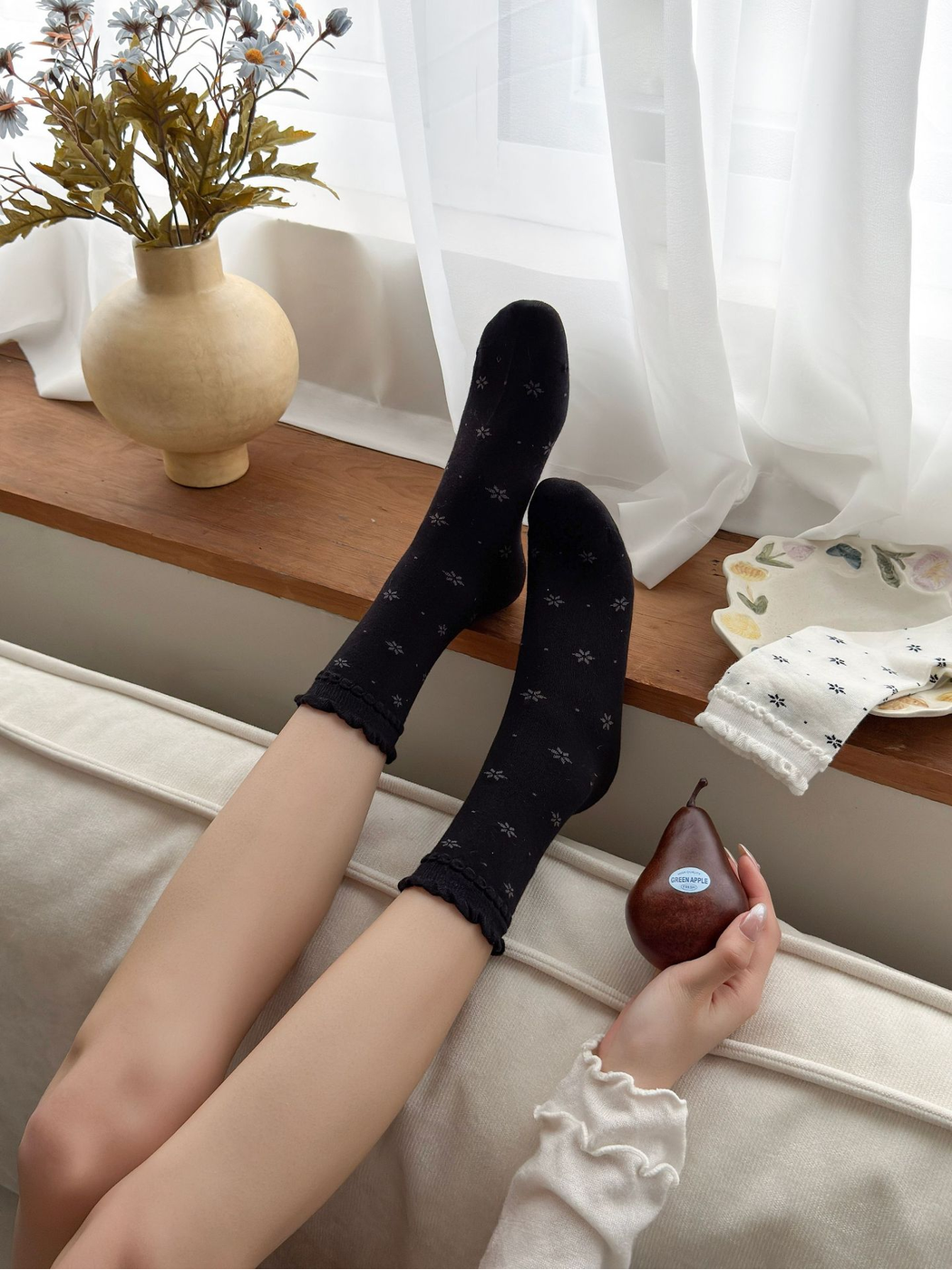 Black floral crew socks worn as a pair in a relaxed seated view
