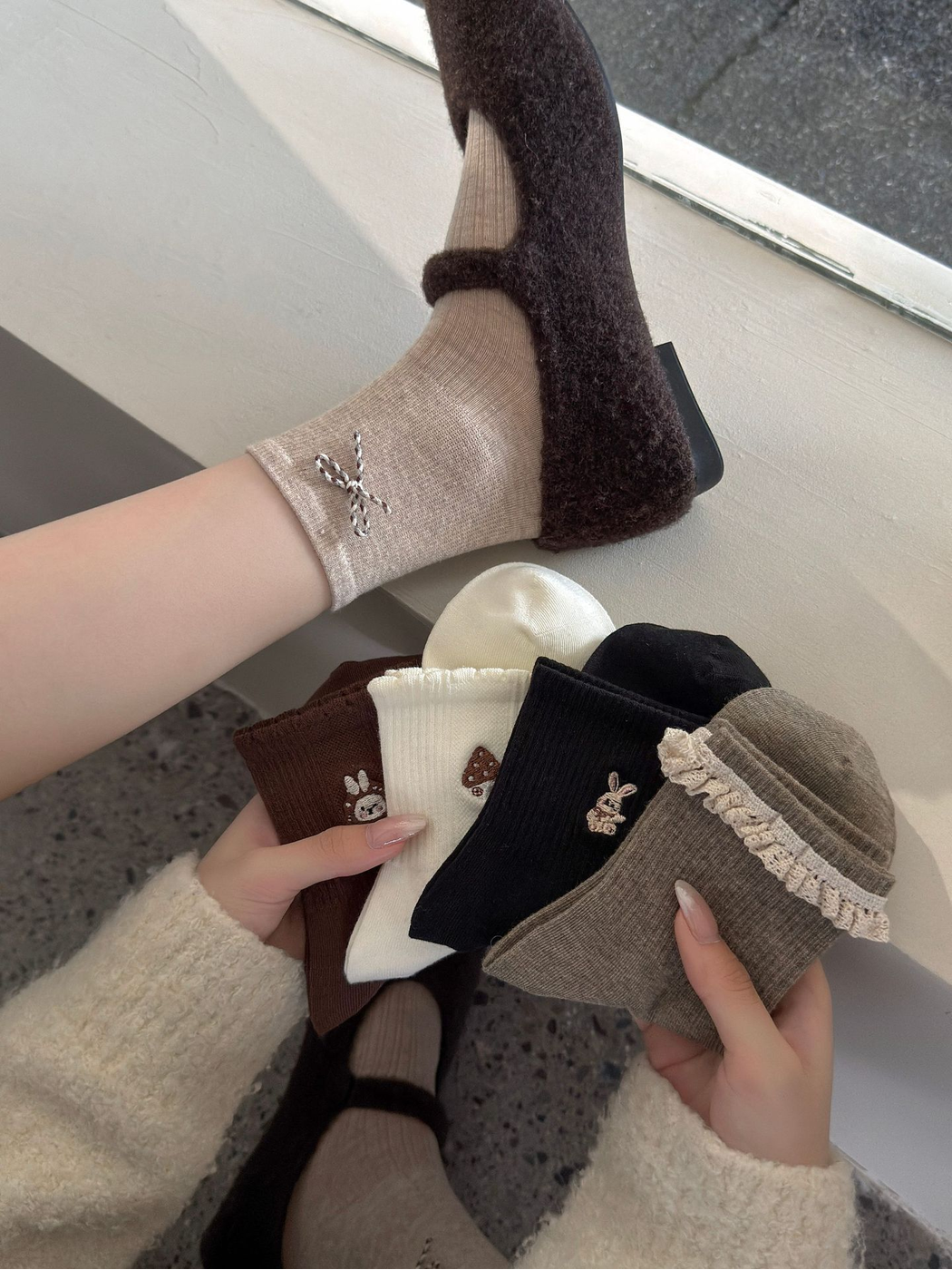 Beige bow socks worn with fuzzy strap shoes beside assorted embroidered socks