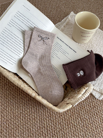 Beige bow and Dark Brown rabbit-face socks arranged in a woven tray