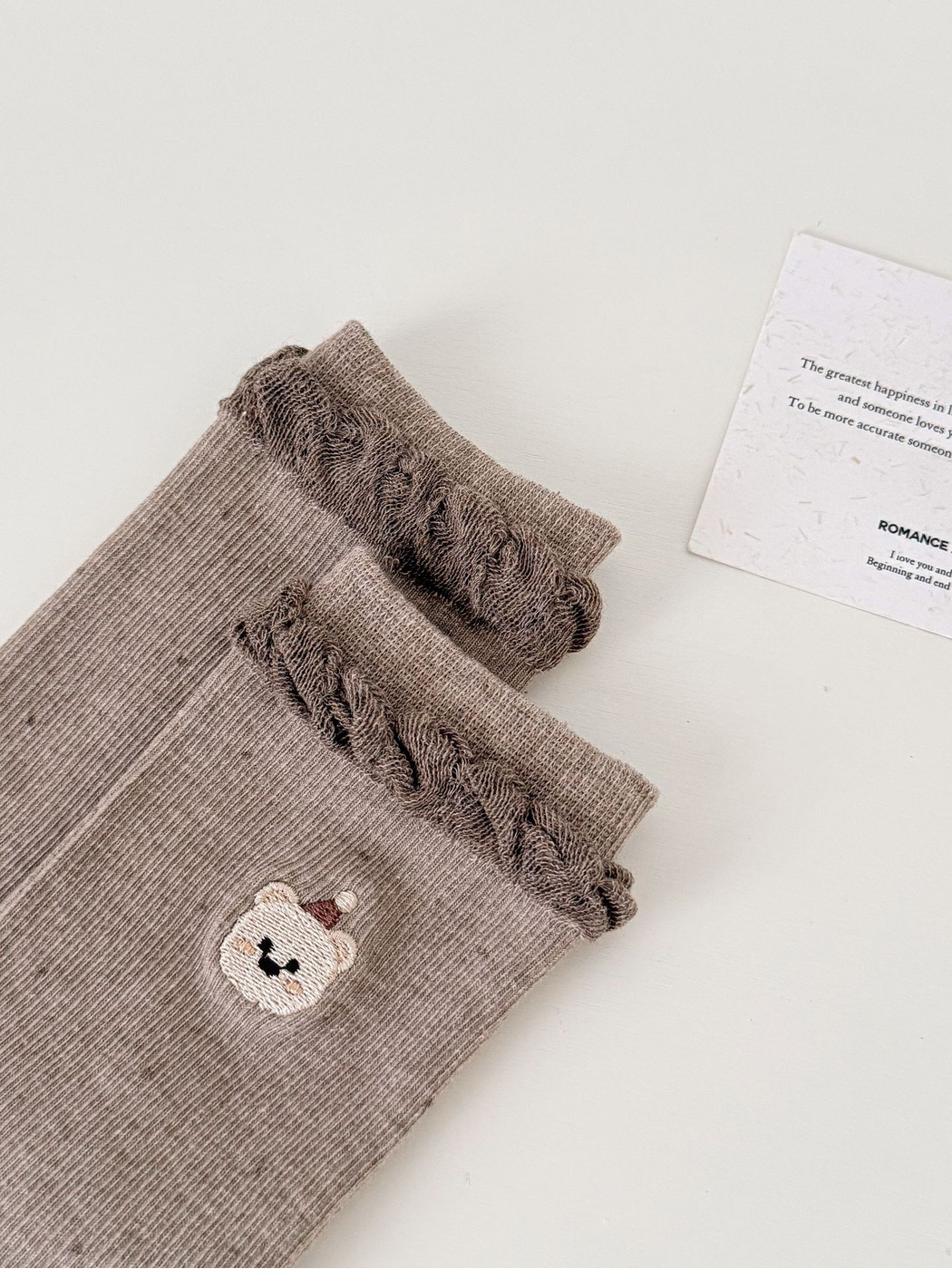 Close-up of a ruffled cuff and embroidered bear face on Light Coffee socks