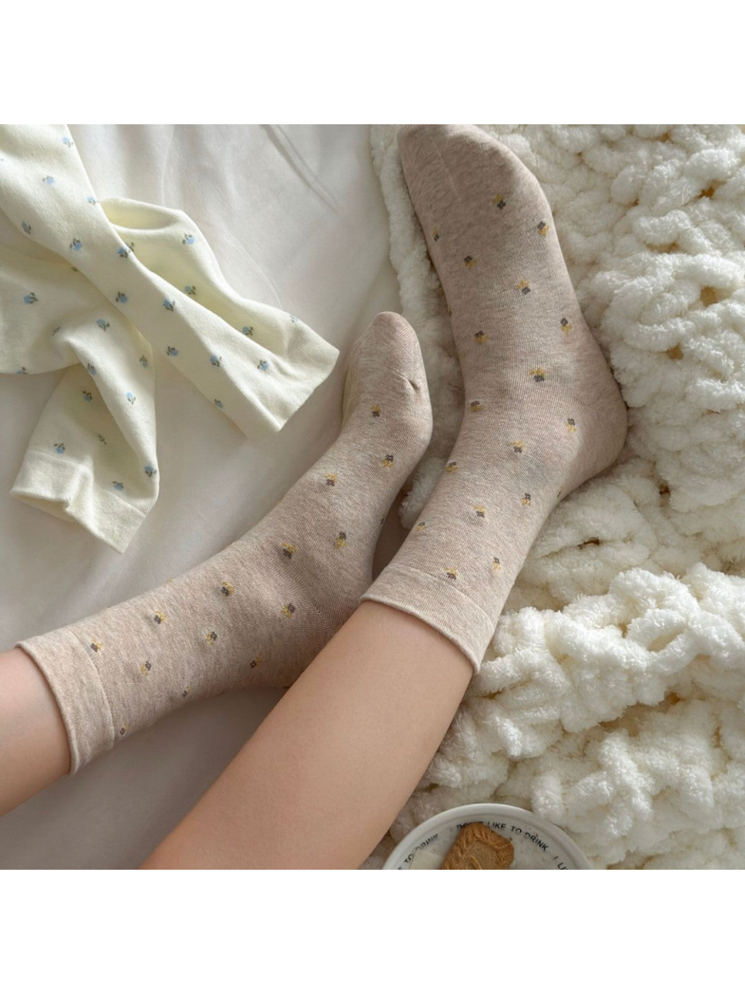 Beige floral crew socks worn while relaxing on a bed