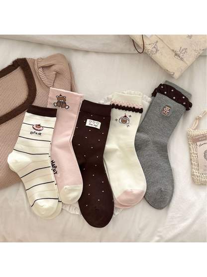 Five bear-themed crew sock styles displayed together in ivory, pink, brown and gray