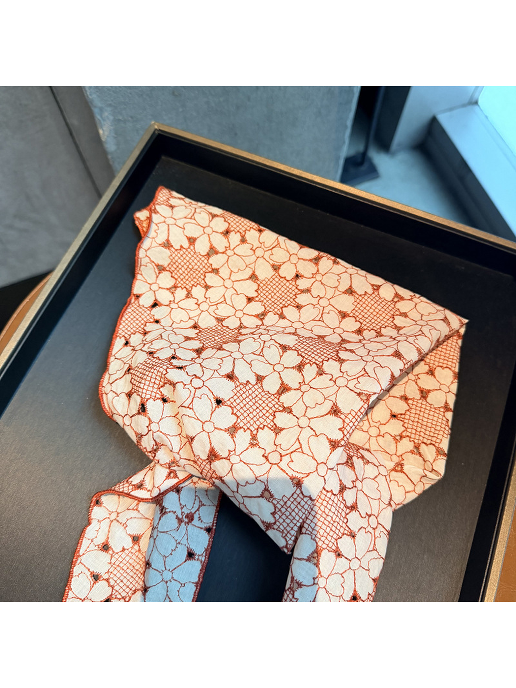 Close-up of the Orange Red floral openwork scarf folded on a black tray
