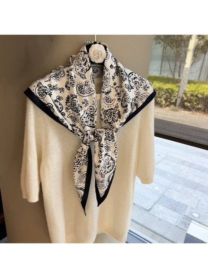 White paisley triangle scarf tied over a cream sweater