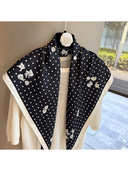 Close view of a black triangle scarf with ivory polka dots, floral clusters and contrasting border