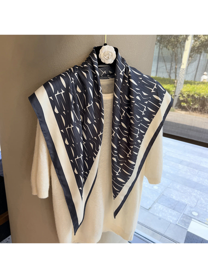 Black and ivory geometric scarf draped over a cream sweater