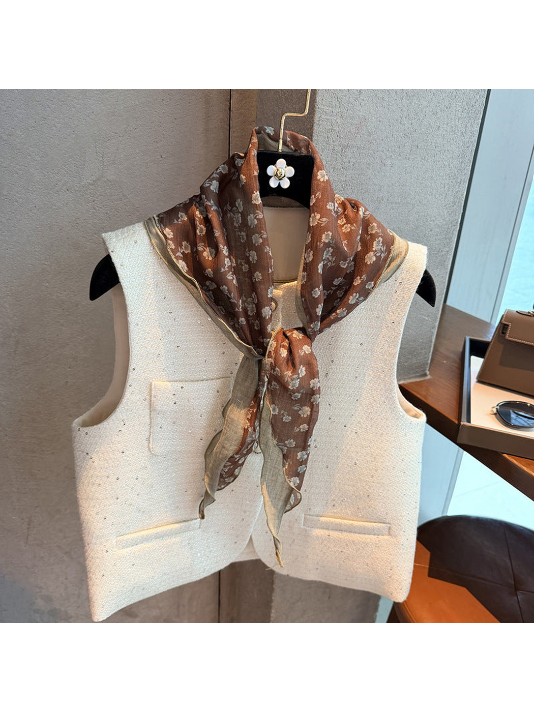 Brown floral triangle scarf knotted over a cream vest