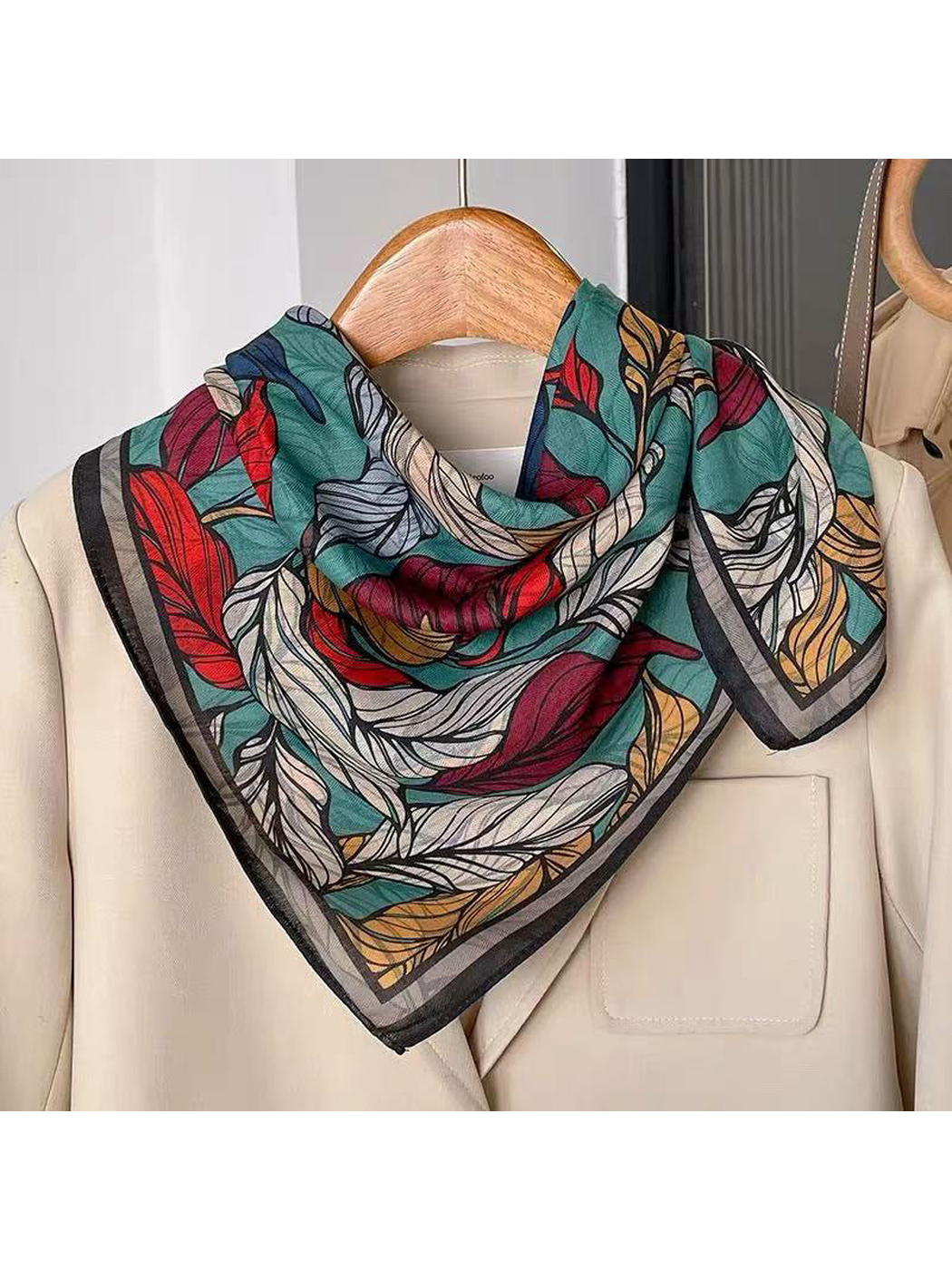 Dark leaf-print square scarf styled over a cream jacket