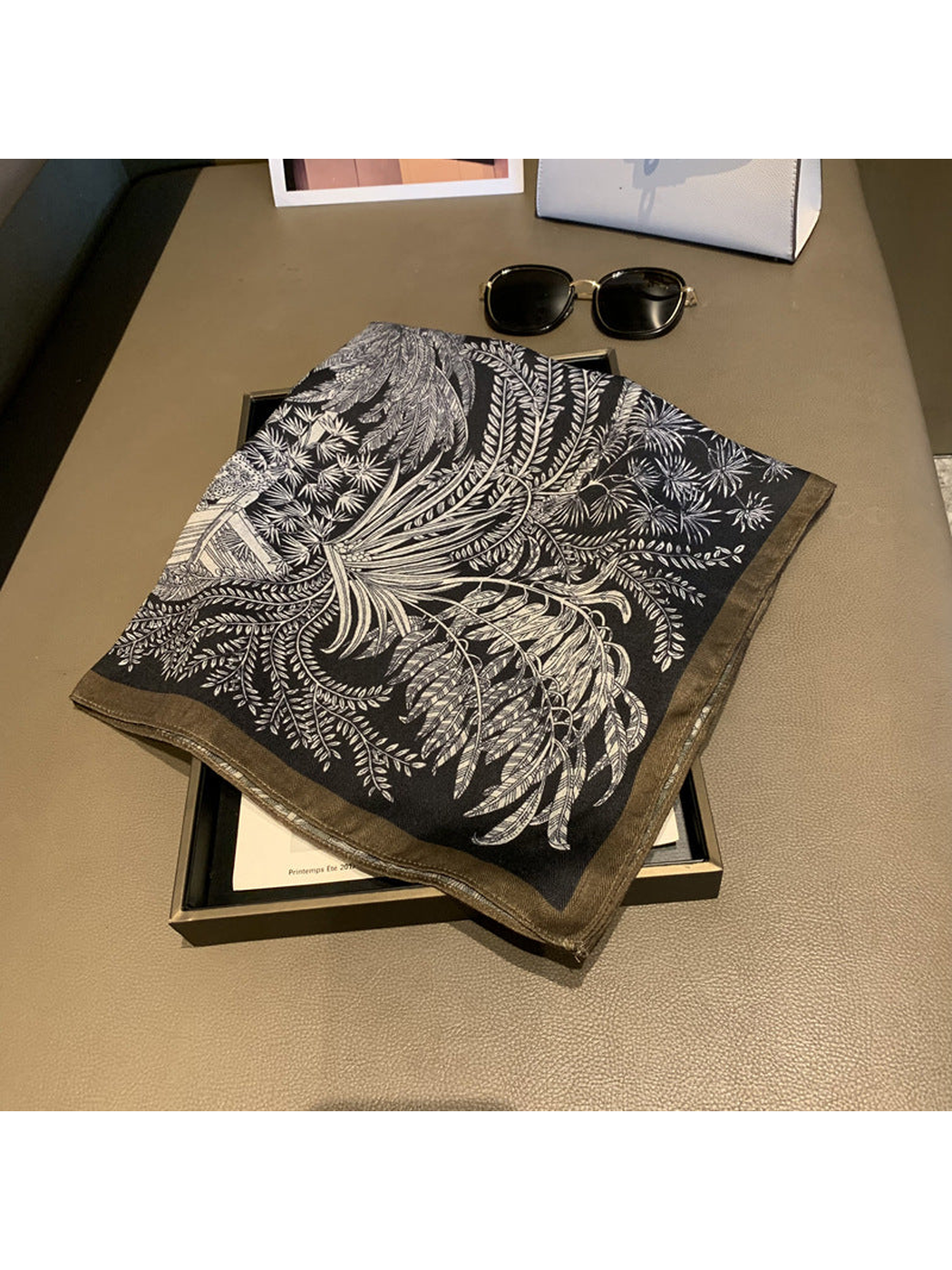 Black square scarf folded to display its botanical print and contrasting border