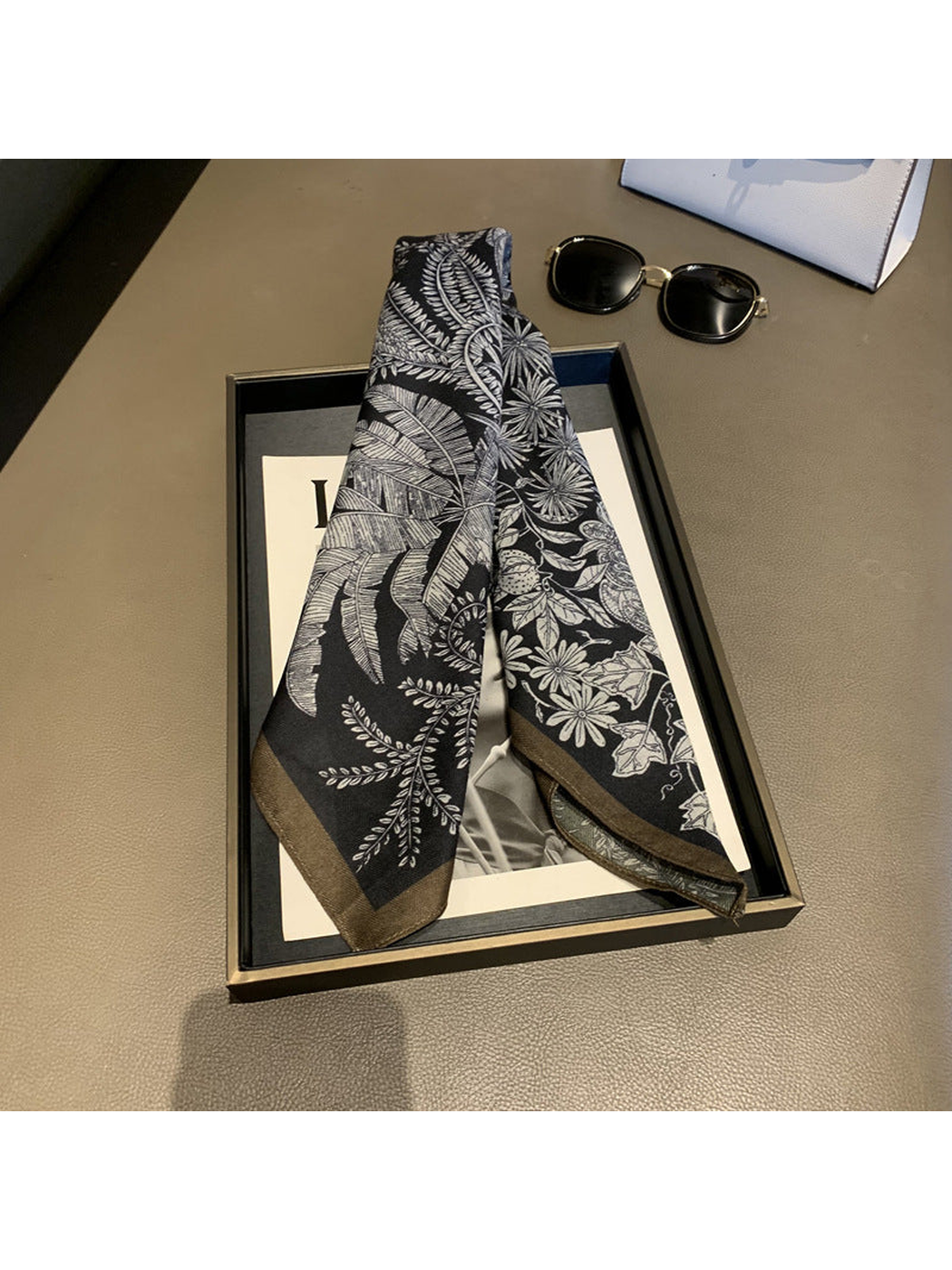 Black scarf draped to show botanical motifs and a contrasting border