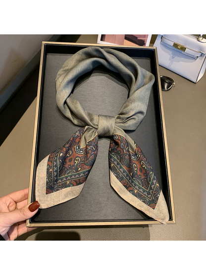 Gray square scarf tied to display its contrasting brown and green paisley ends