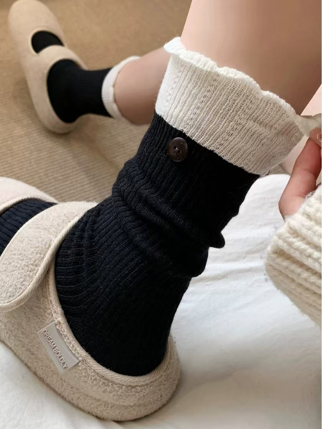 Close-up of a black ribbed sock with ivory ruffled cuff and button accent