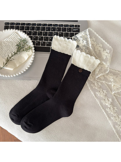 Black ribbed crew socks with ivory ruffled cuffs arranged beside a laptop and lace