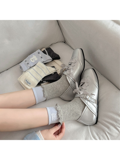 Gray ruffled crew socks layered over light blue bow socks and styled with silver shoes