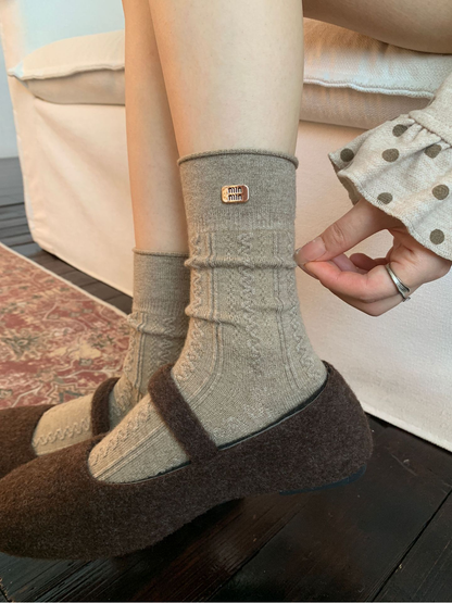 Close-up of greige Cable crew socks with rolled edges and textured panels