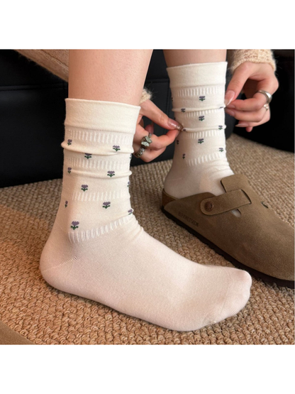 Ivory crew socks with miniature purple flower motifs, worn without shoes