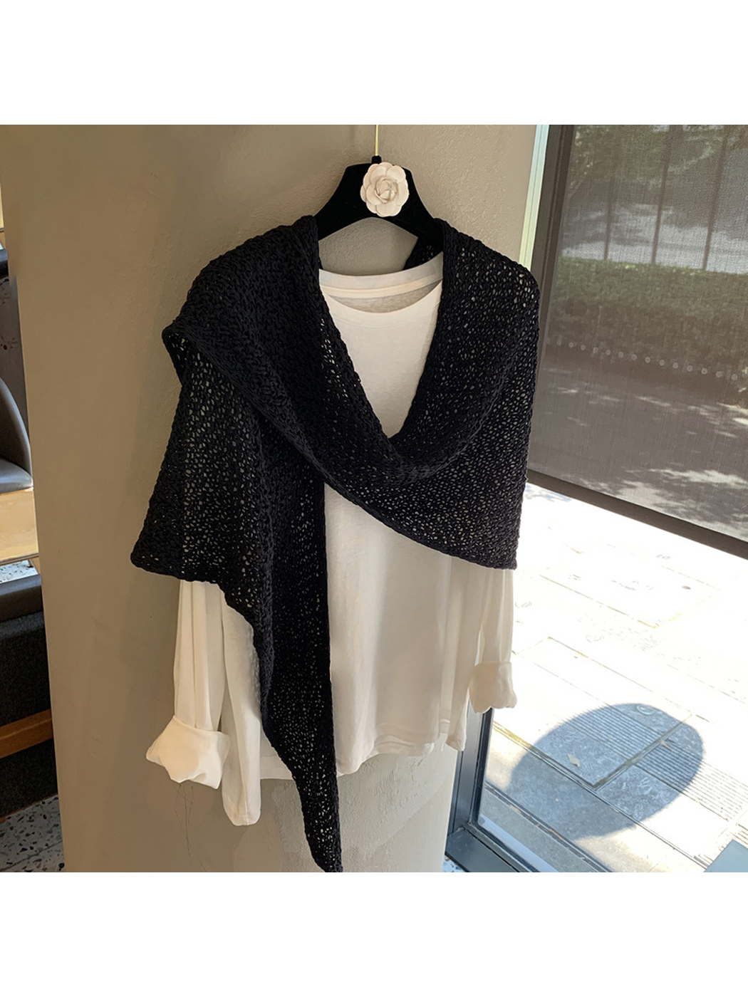 Black openwork triangle scarf crossed over the shoulders of a white top