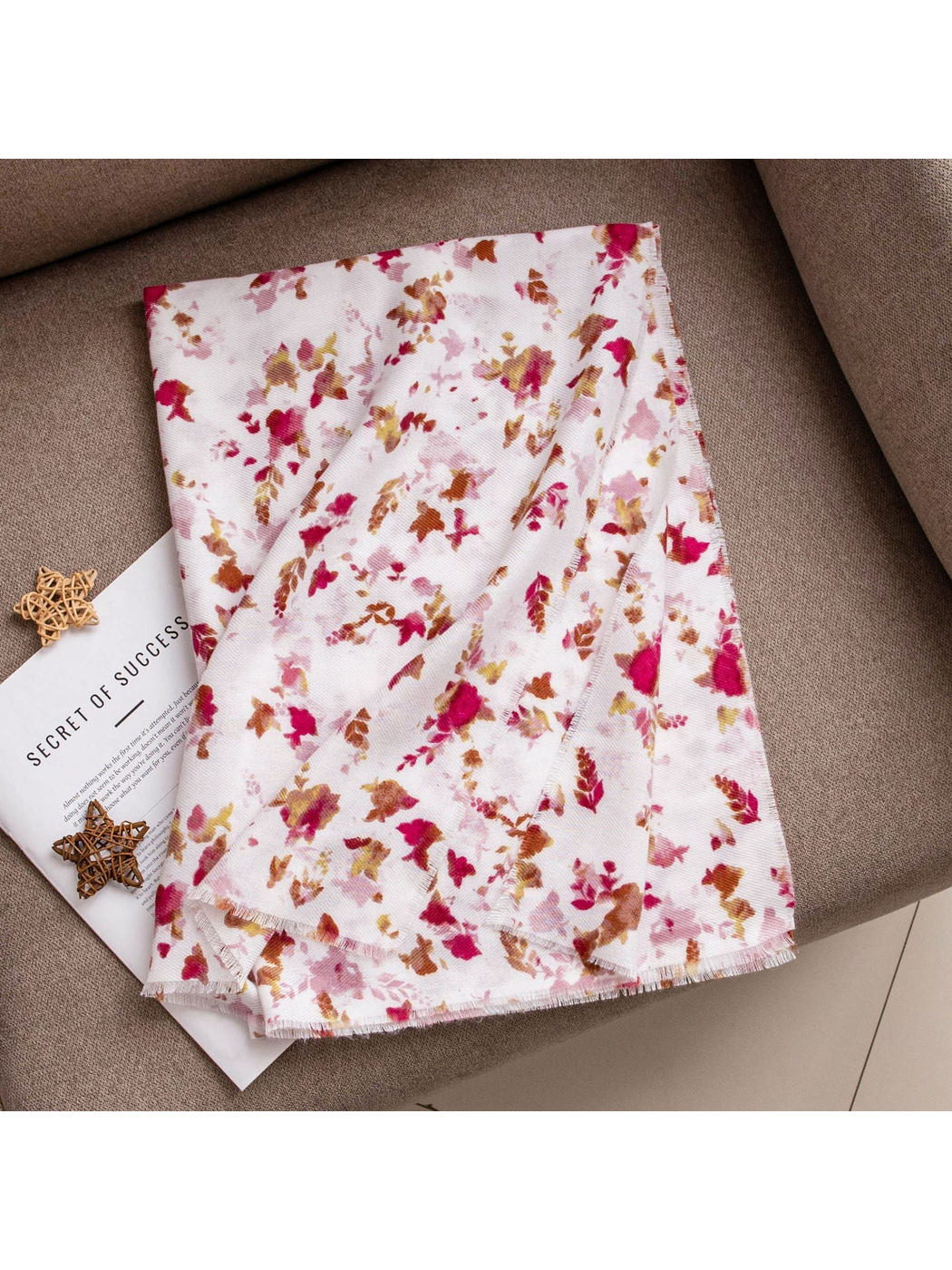 Ivory floral scarf loosely folded on a brown upholstered surface