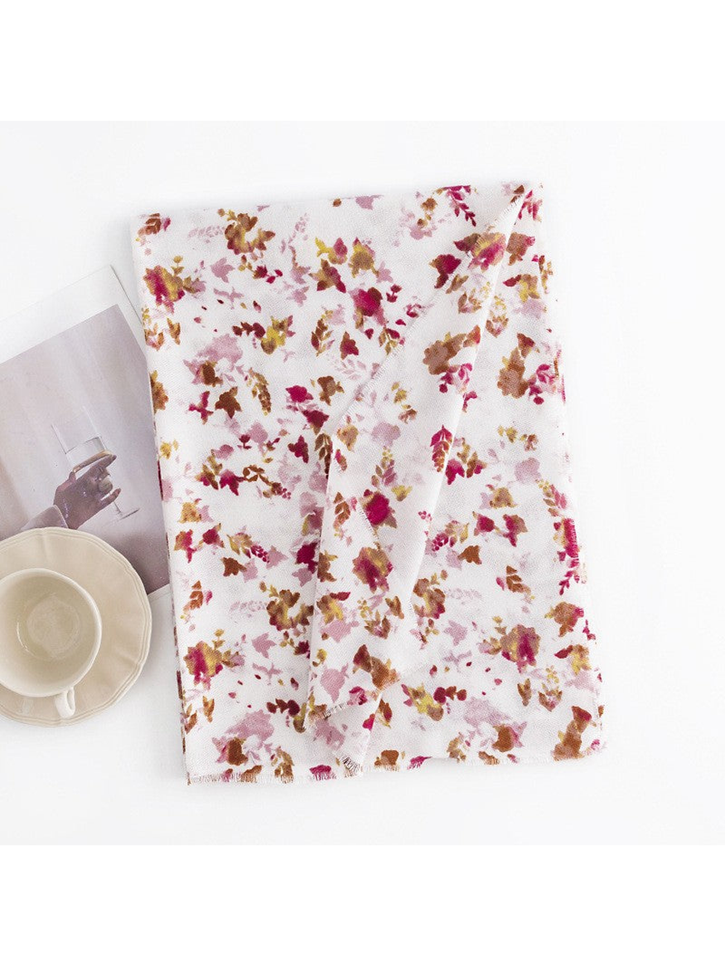 Ivory floral scarf folded beside a cup and decorative print