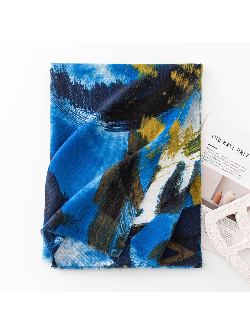 Blue abstract brushstroke scarf folded beside a magazine