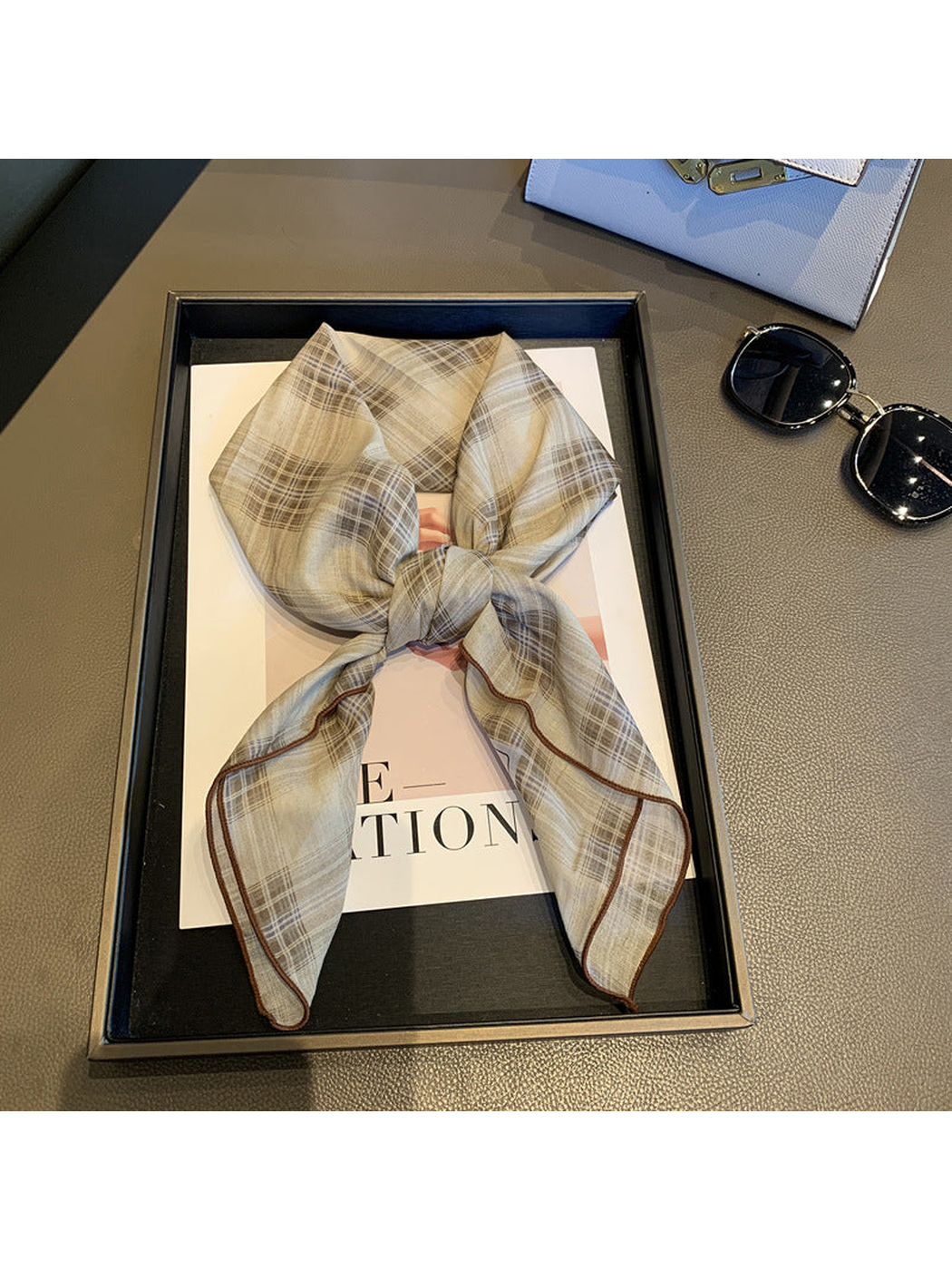 Greige plaid scarf tied in a loose knot with brown edging