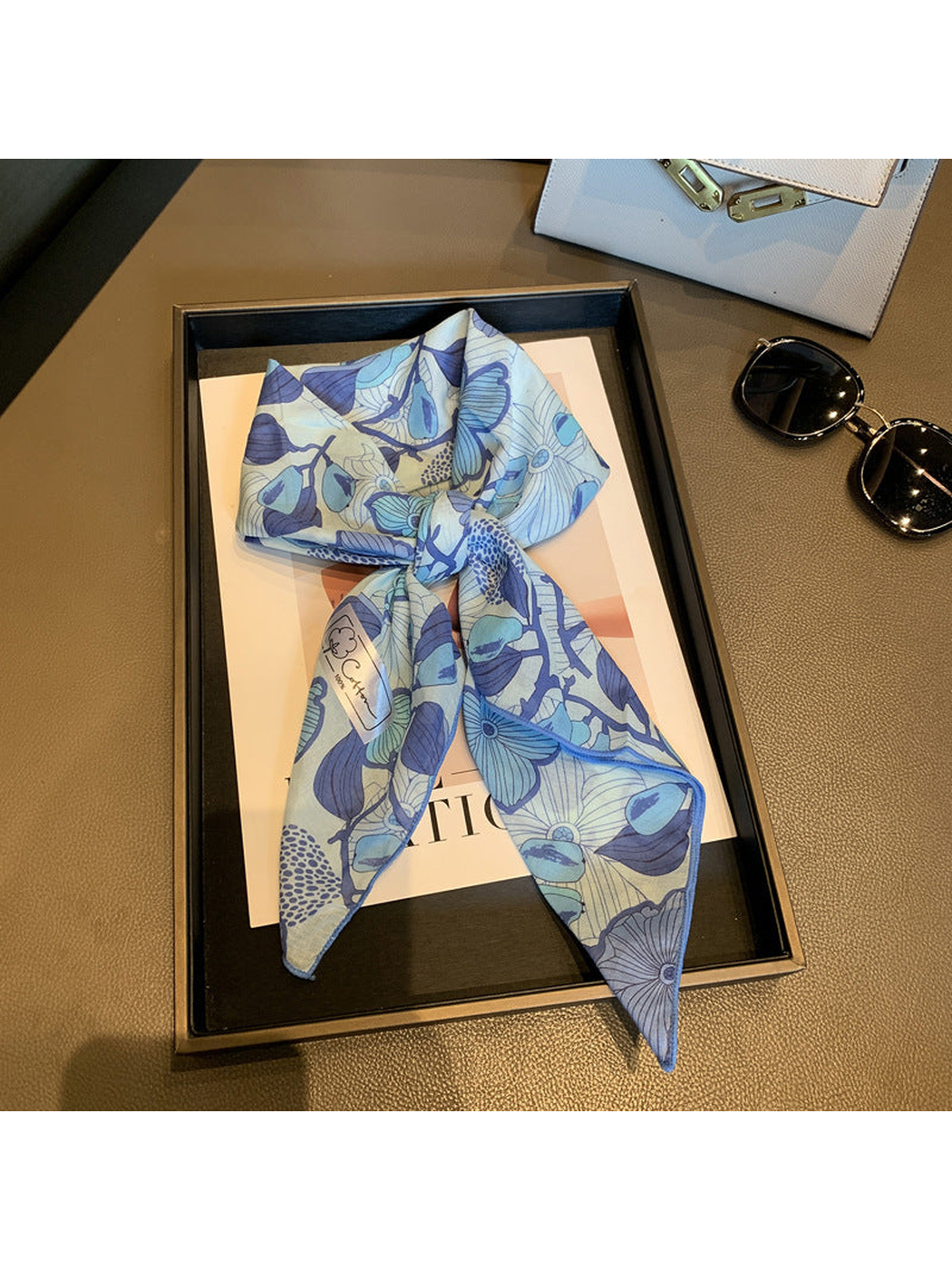 Blue floral square scarf tied in a loose knot on a display tray
