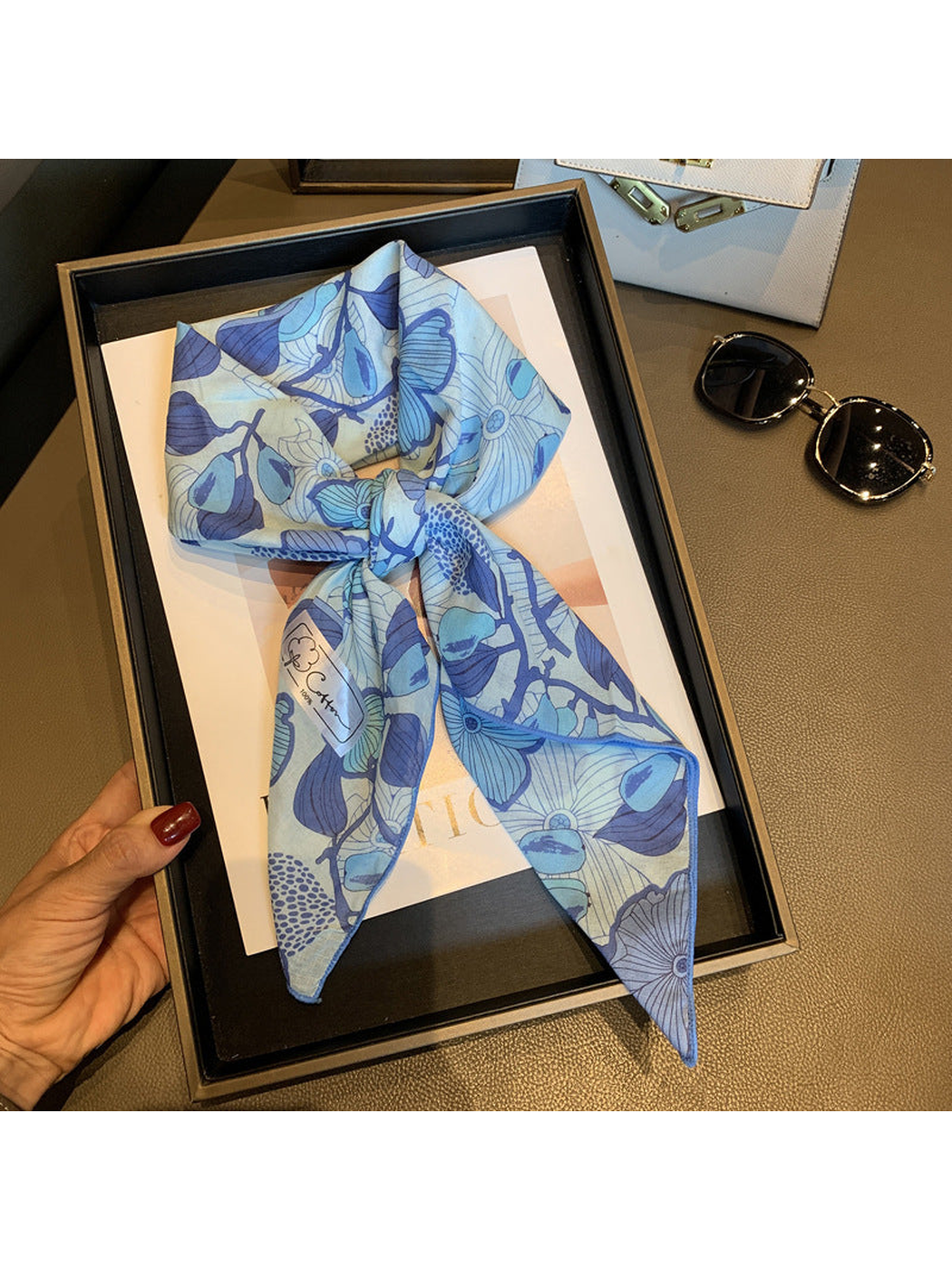 Blue floral square scarf arranged in a loose knot and held on a display tray
