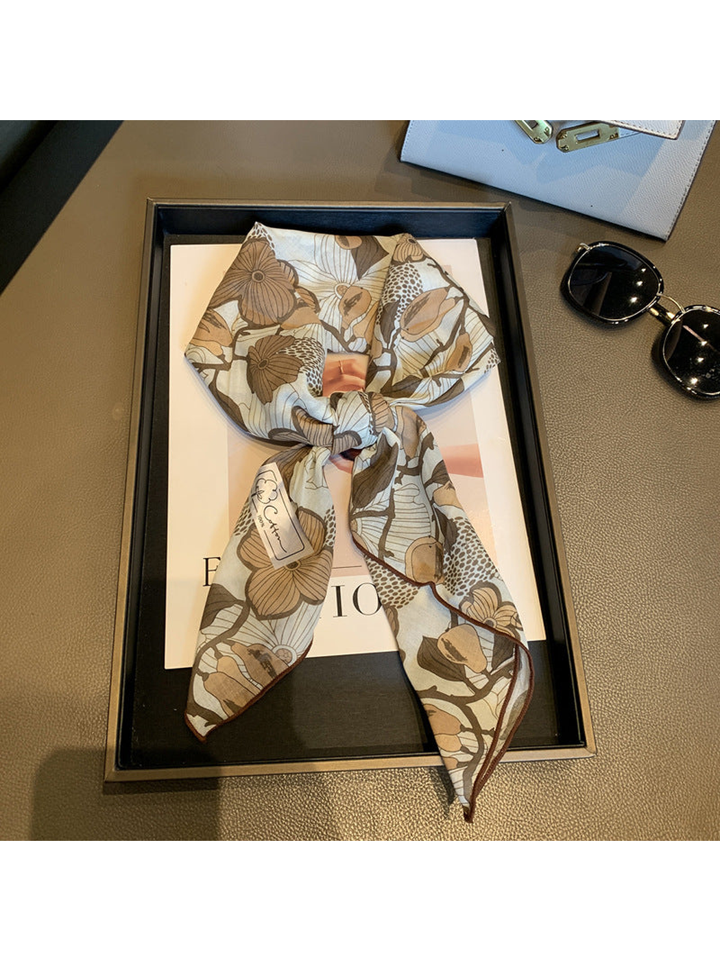 Khaki floral square scarf tied in a loose knot on a display tray