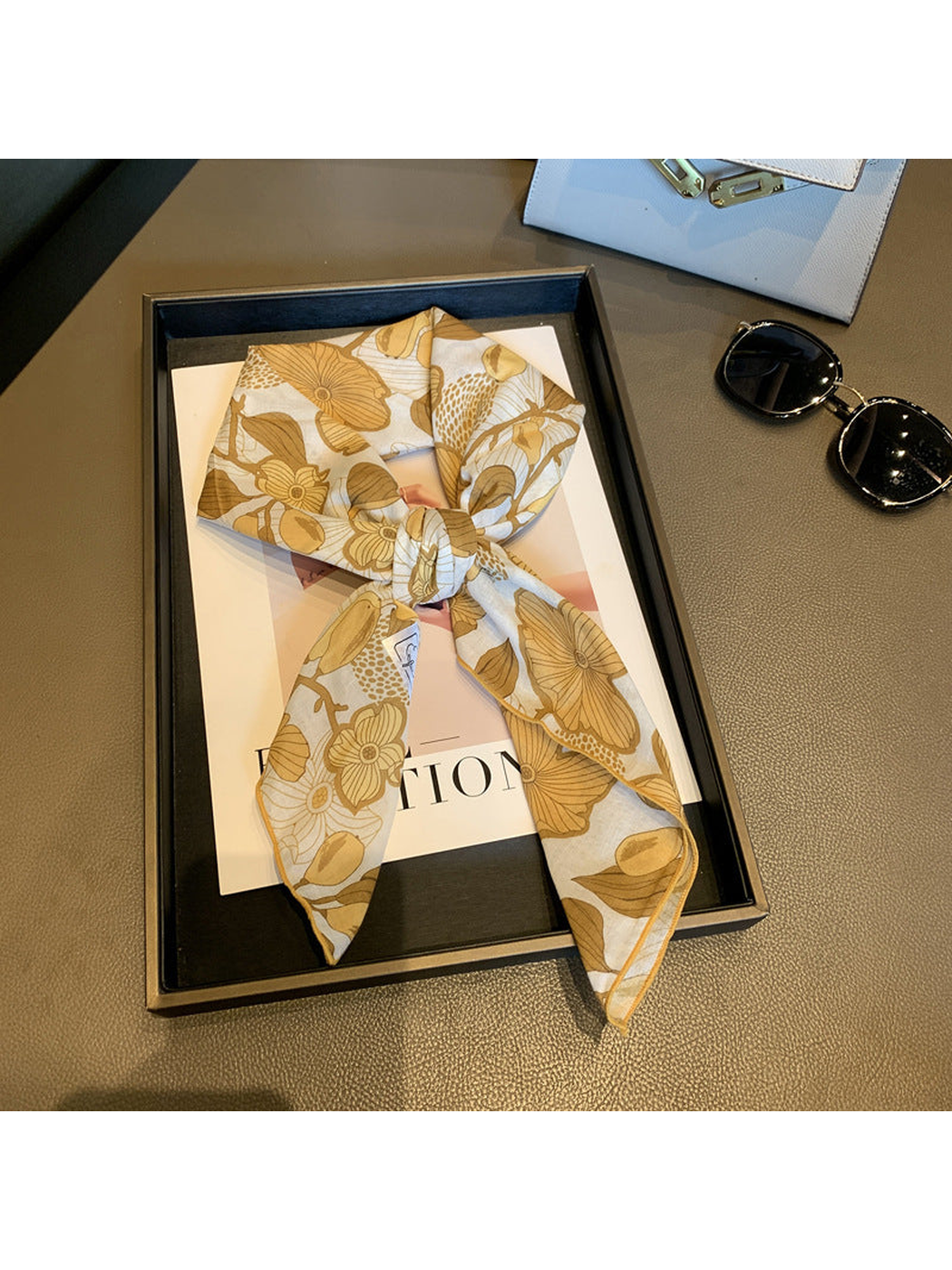 Beige floral square scarf tied in a loose knot on a display tray