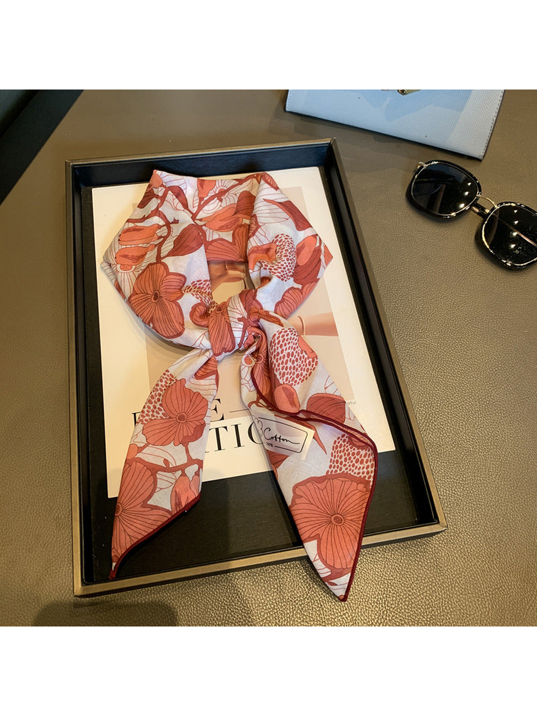 Red floral square scarf tied in a loose knot on a display tray