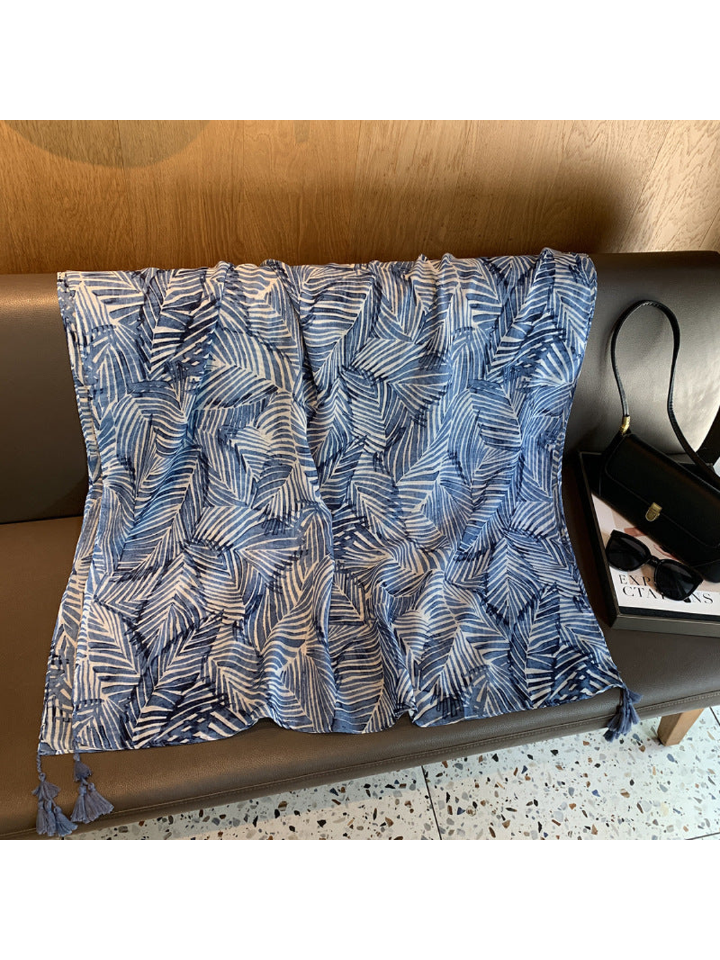Blue rectangular leaf-pattern scarf draped flat with corner tassels visible