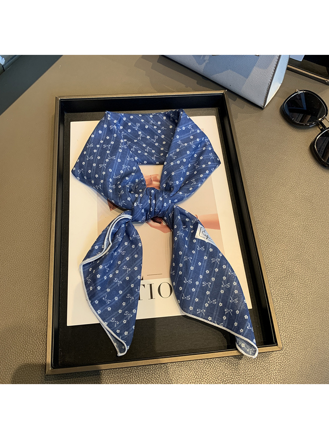 Navy bow-and-flower square scarf tied in a loose knot