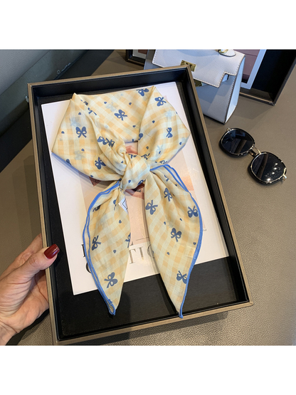 Yellow gingham scarf with blue bow motifs tied and held in a tray